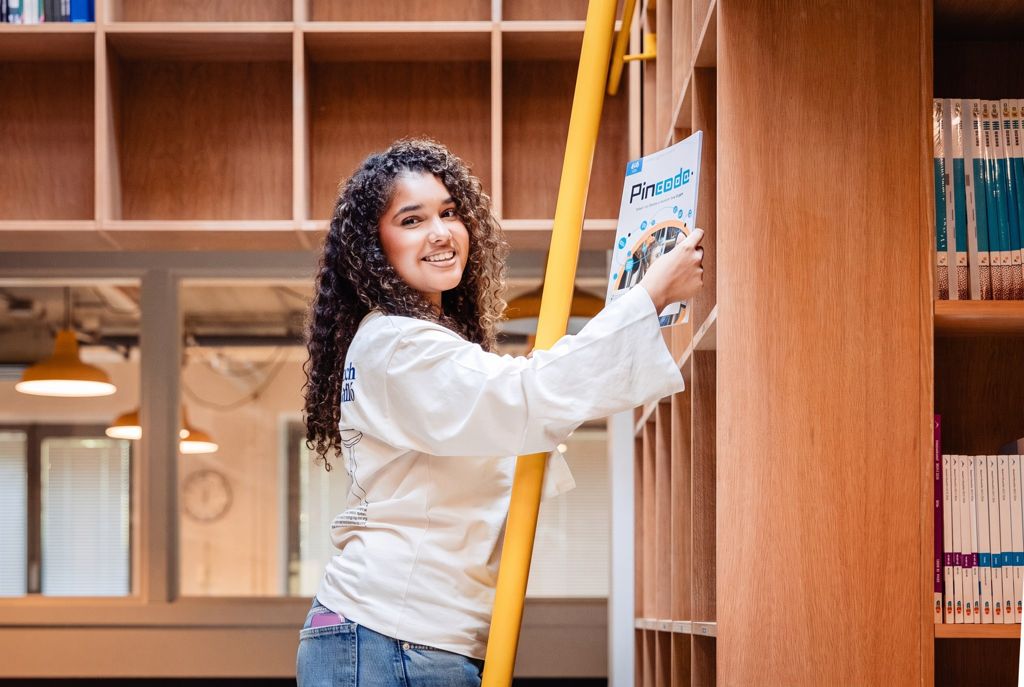 Een leerling zet bij de gele ladder een boek terug in de boekenkast van de bibliotheek