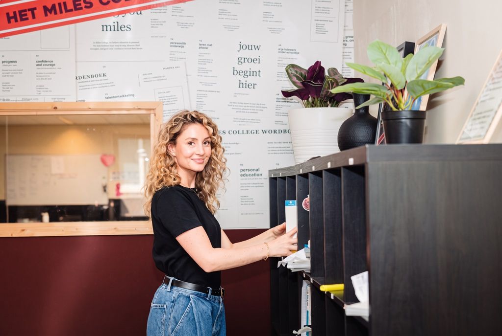 Een medewerker sorteert post bij de postvakken, voor een wand met het Miles-woordenboek