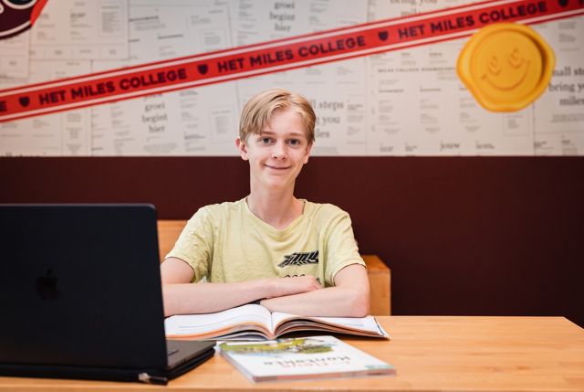 Een leerling werkt aan een laptop met een boek naast zich