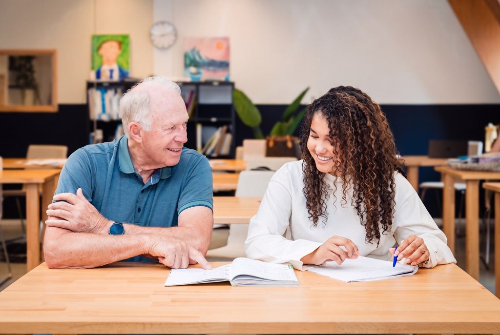 Een mentor en een leerling lachen samen boven een opengeslagen boek