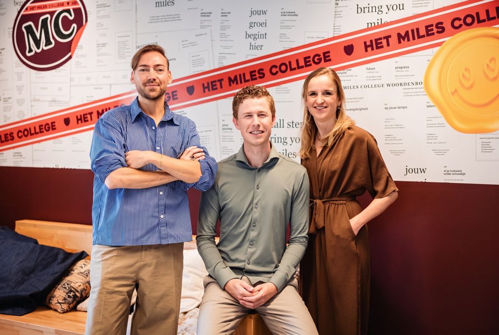 Drie teamleden staan voor een muur met het rode Miles-lint