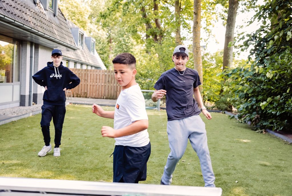 Drie leerlingen voetballen op het kunstgras in de tuin naast het schoolgebouw